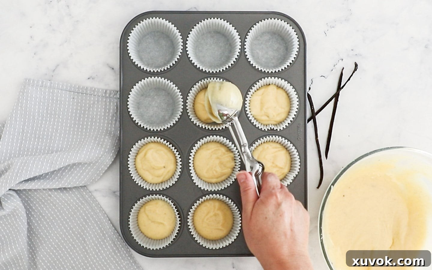 Cupcake batter being scooped into paper cases in a muffin pan.