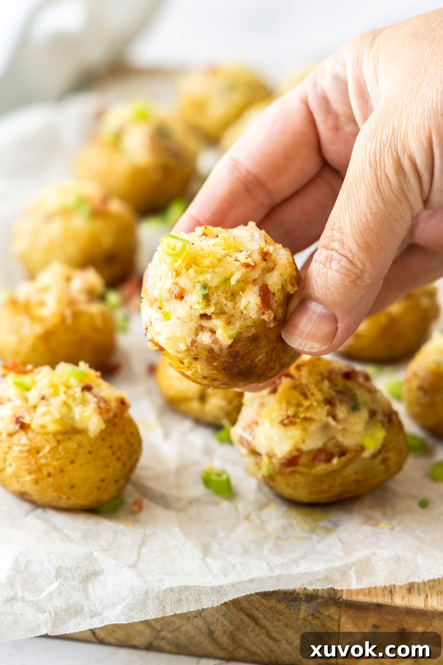 A hand holding a perfectly golden and filled mini loaded potato, ready to be eaten.