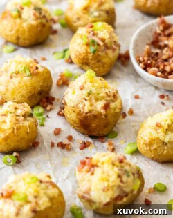 A whole batch of mini baked potatoes with bits of bacon scattered around.