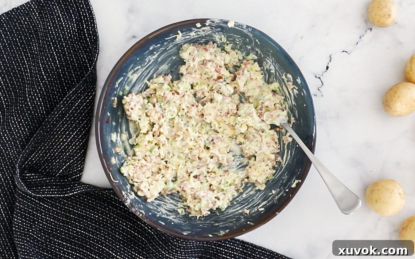 A bowl containing the mixed filling ingredients: bacon, spring onion, sour cream, cheddar, and melted butter.