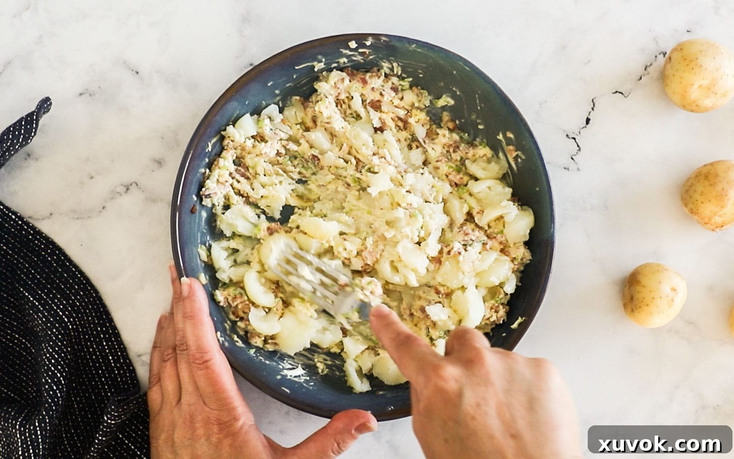 Mashing the scooped potato insides into the filling mixture in a bowl.