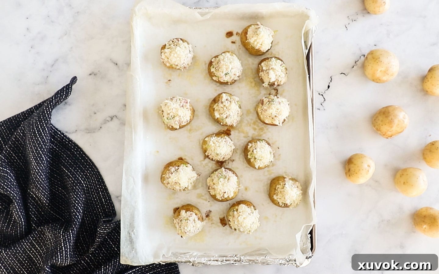 Filled mini baked potatoes, topped with parmesan and breadcrumbs, arranged on a baking tray.