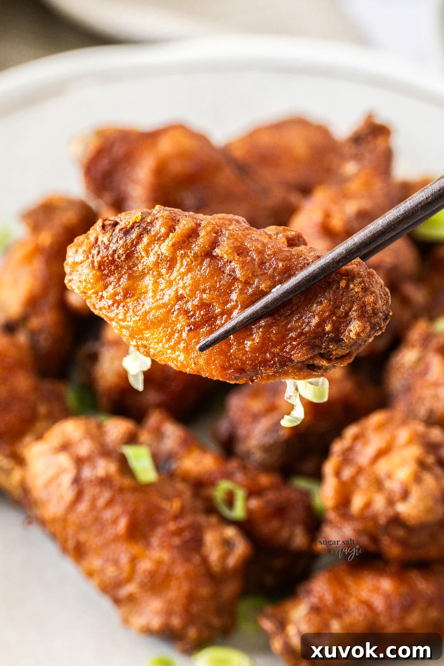 A single Chinese fried chicken wing held by chopsticks, showcasing its golden, crispy exterior.