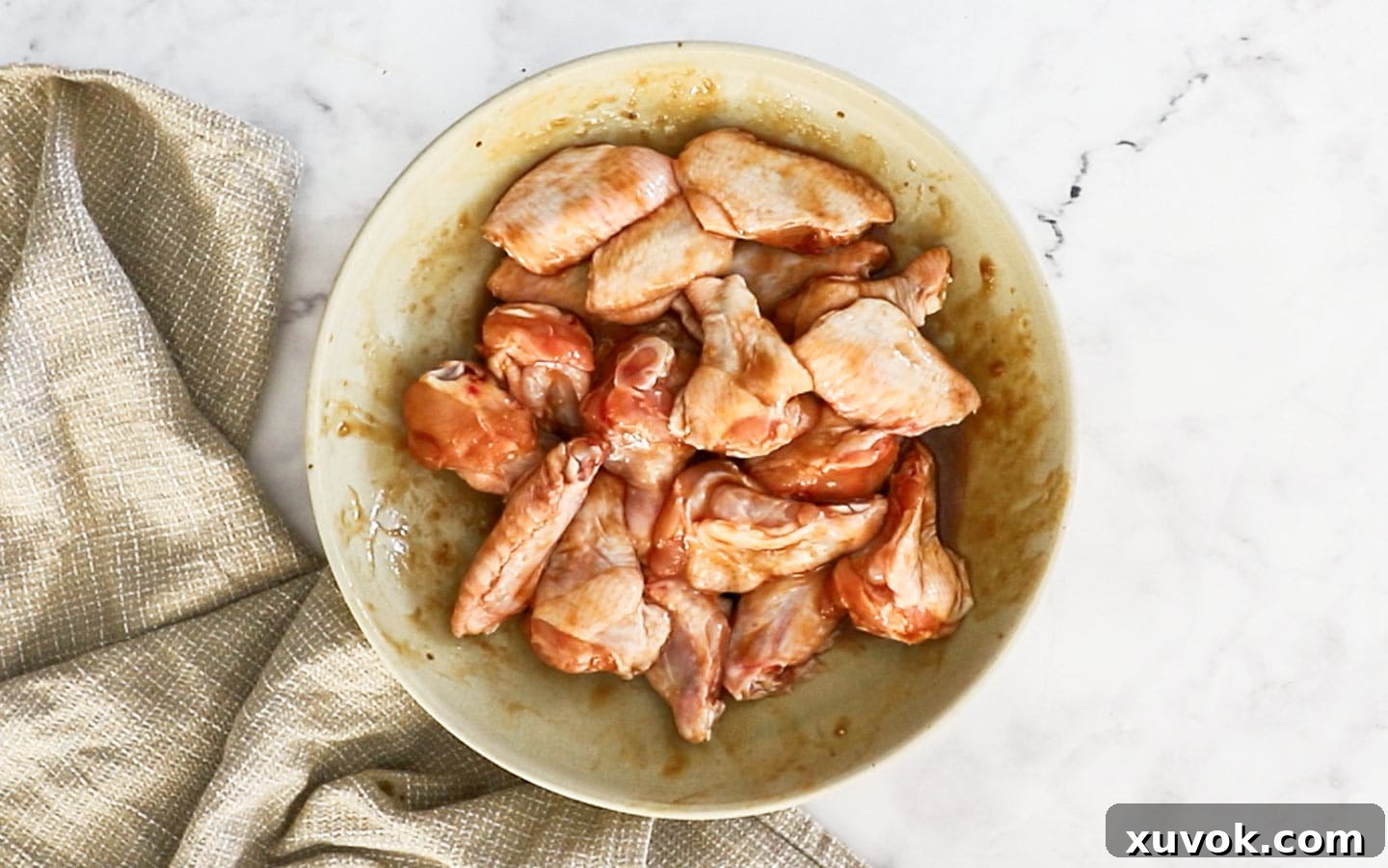 Chicken wings thoroughly mixed in a bowl with the rich, savory marinade.