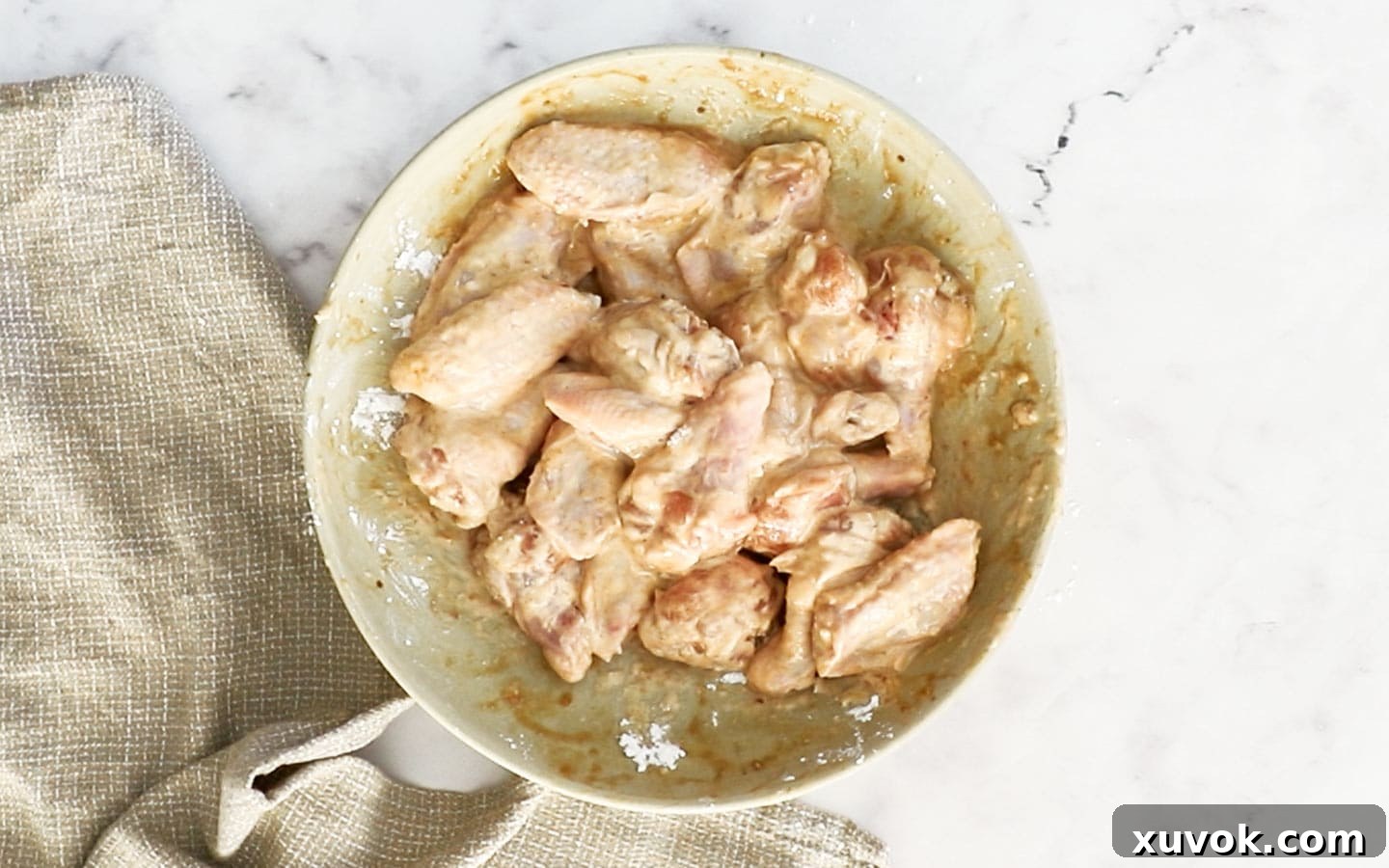 Marinated chicken wings in a bowl, now coated with a white powder mixture of cornflour and baking powder.