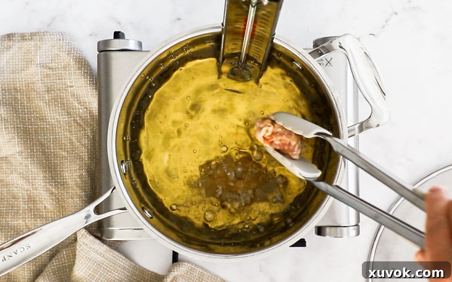A hand gently placing individual chicken wing pieces into a pan of hot, bubbling oil for the first fry.