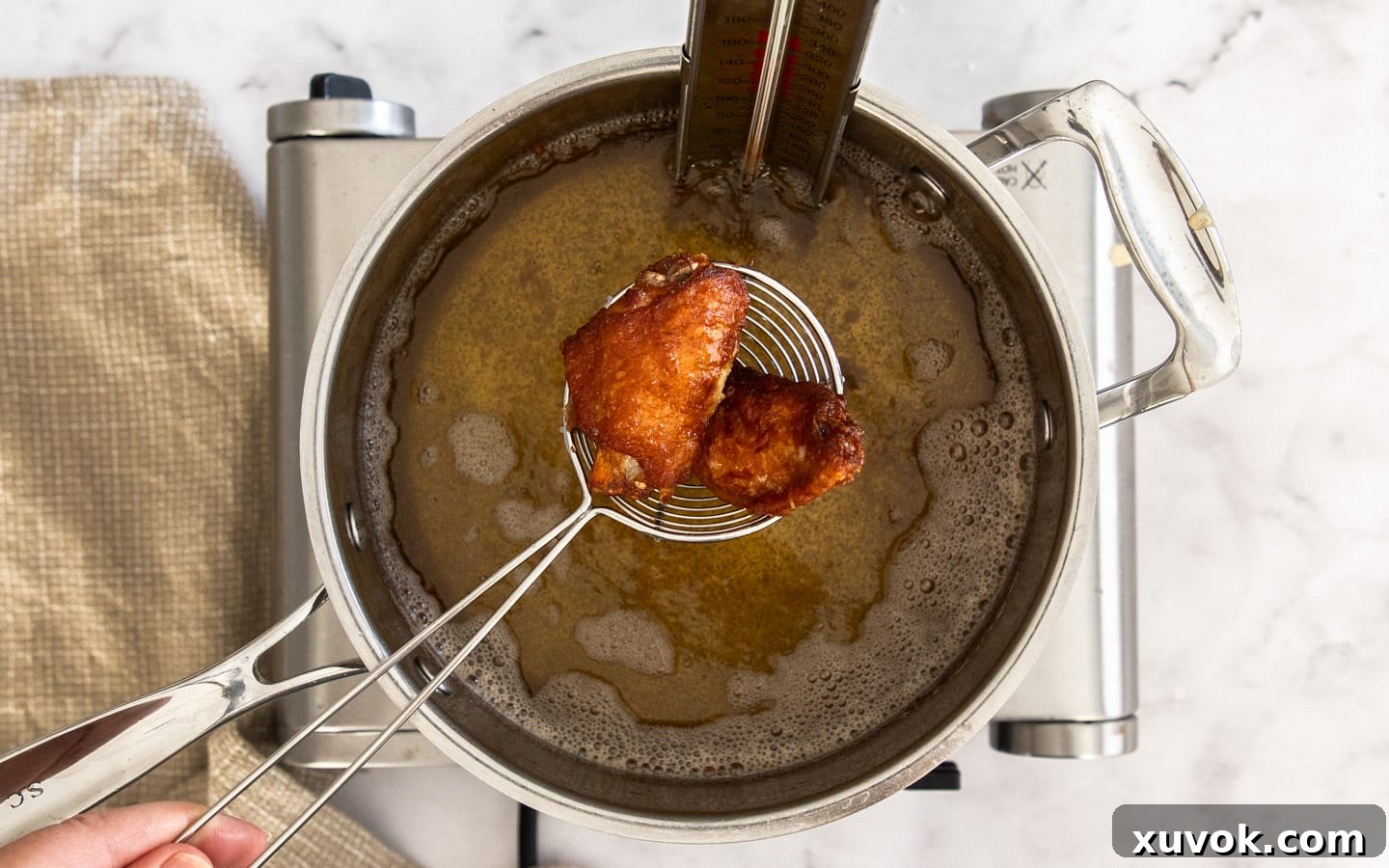 Two perfectly fried Chinese chicken wing pieces being carefully removed from hot oil with a wire skimmer.