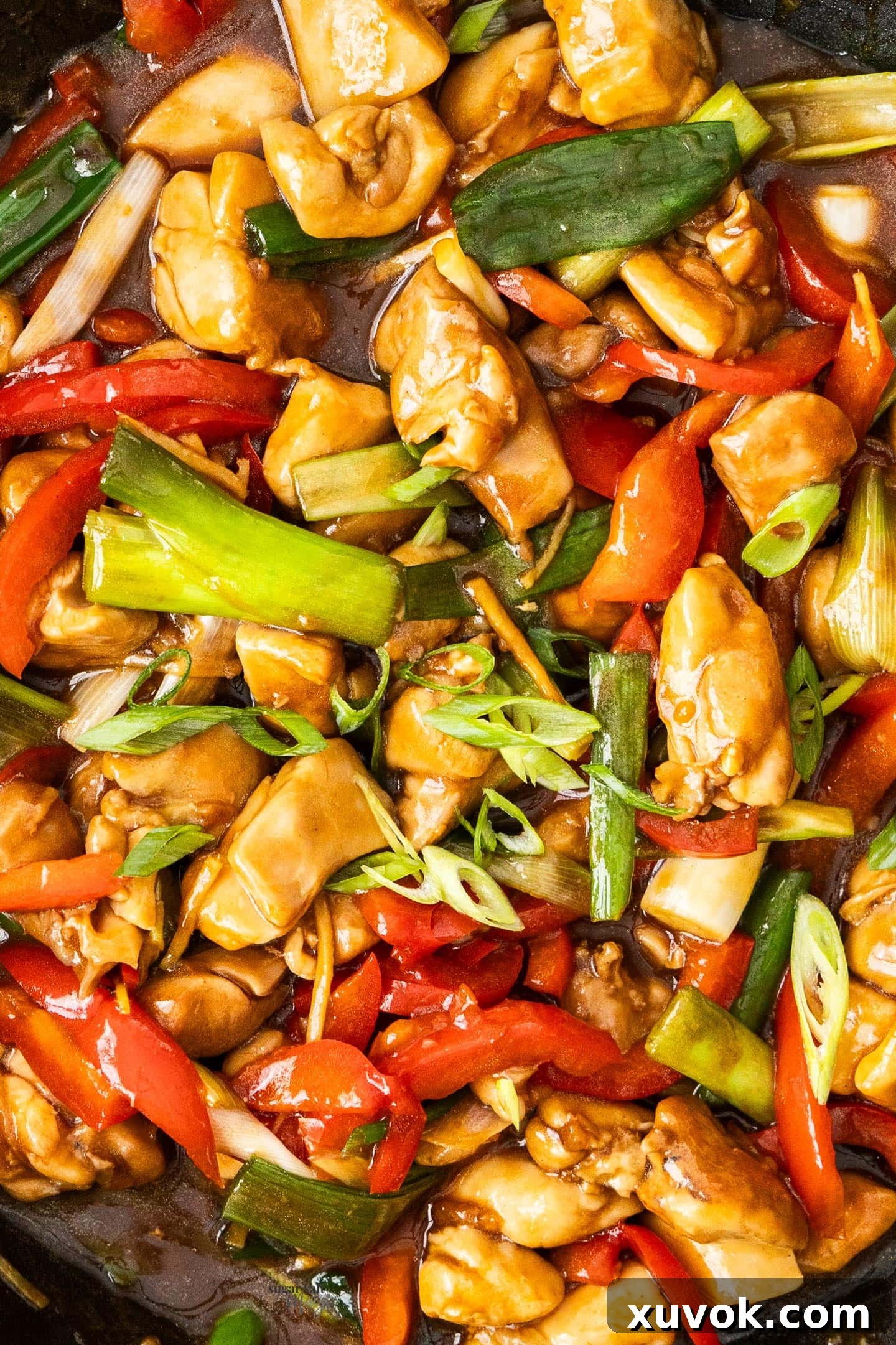 Extreme closeup of chicken and vegetables coated in oyster sauce in a wok, highlighting the texture and glaze.