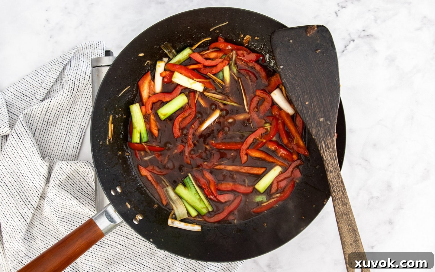 The glossy sauce being added to the stir-frying vegetables in the wok.