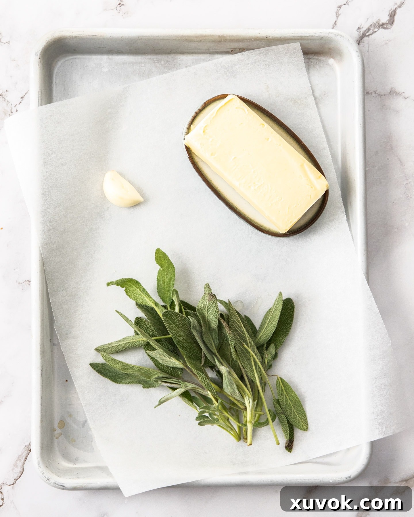 Ingredients for sage butter sauce on a baking tray including butter, garlic, and fresh sage.