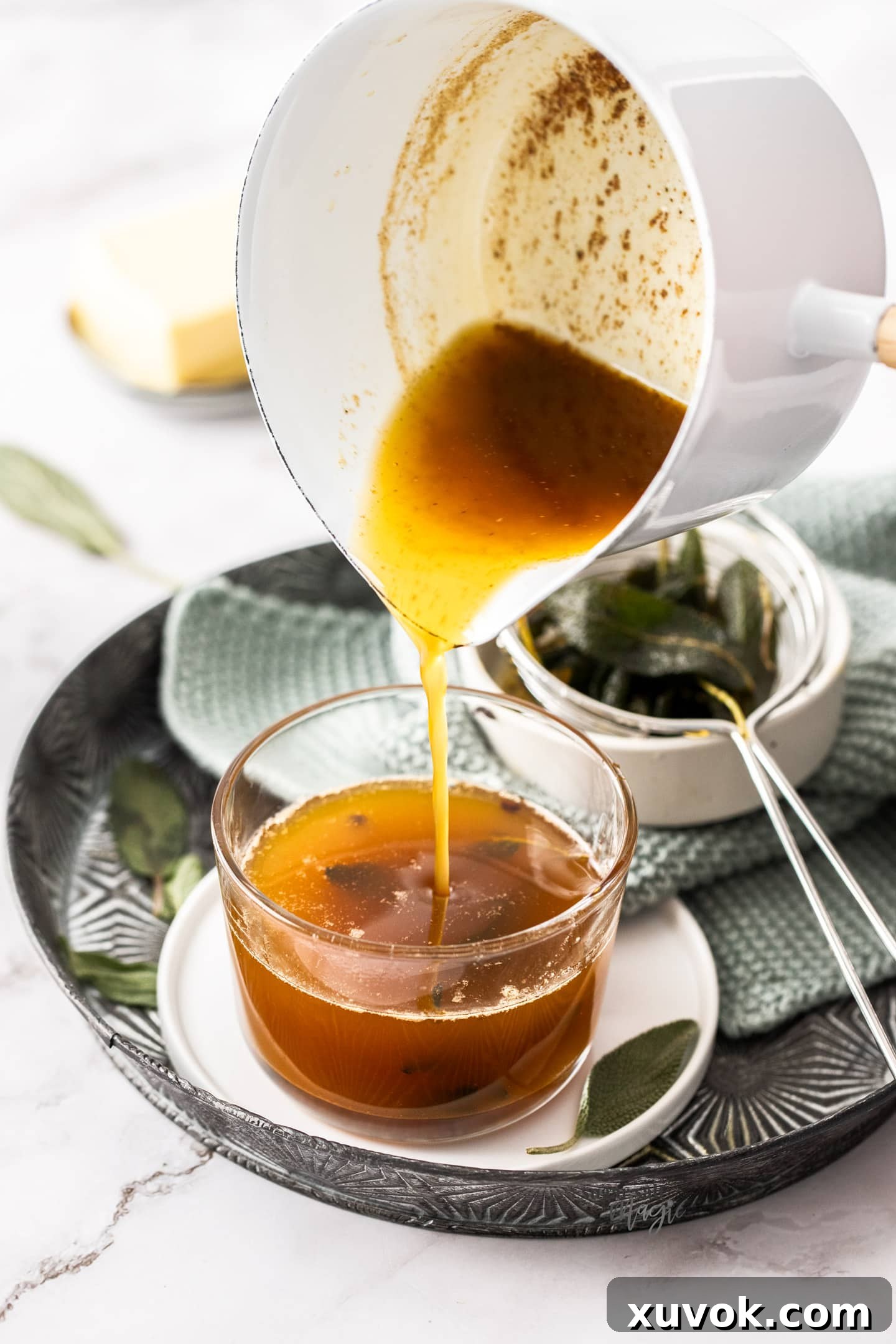 Pouring the amber sage butter sauce into a glass for serving or storage.