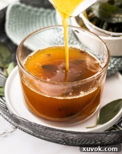 Closeup of pouring the brown butter sage sauce into a glass, highlighting its amber color and crispy sage.