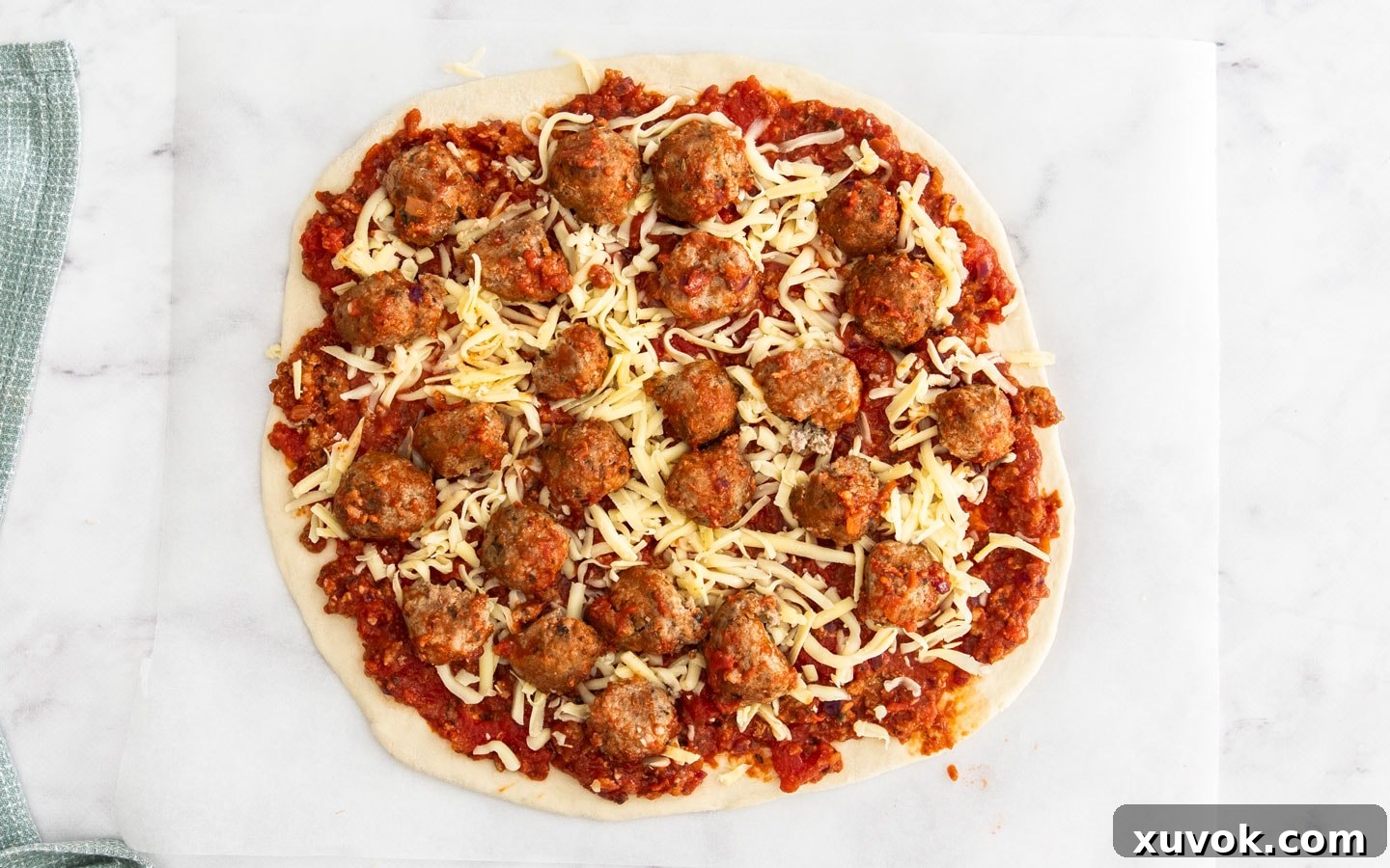 The pizza base topped with sauce, cheese and meatballs.