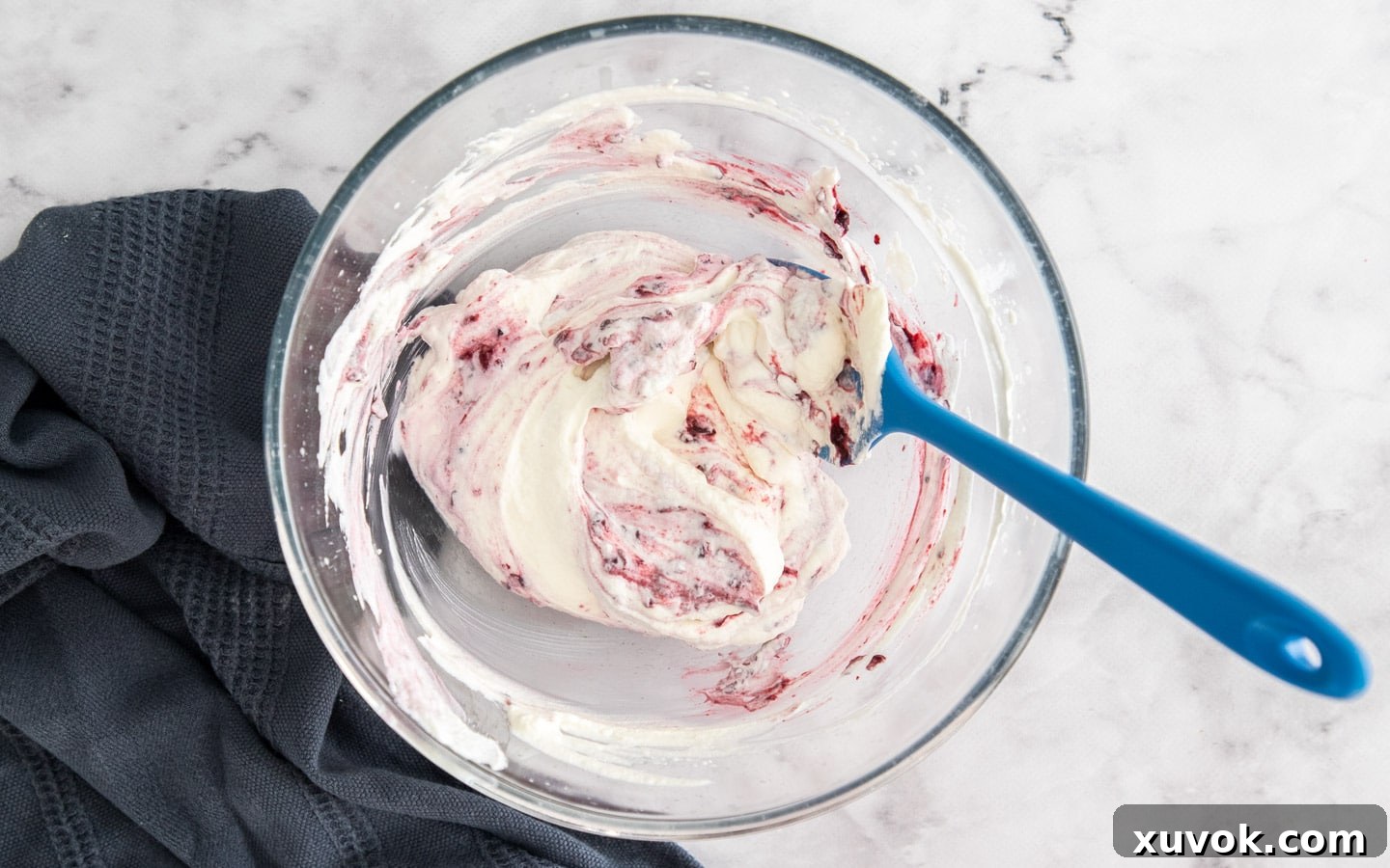 A vibrant blackberry compote being gently swirled through fluffy whipped cream, creating a marbled effect.