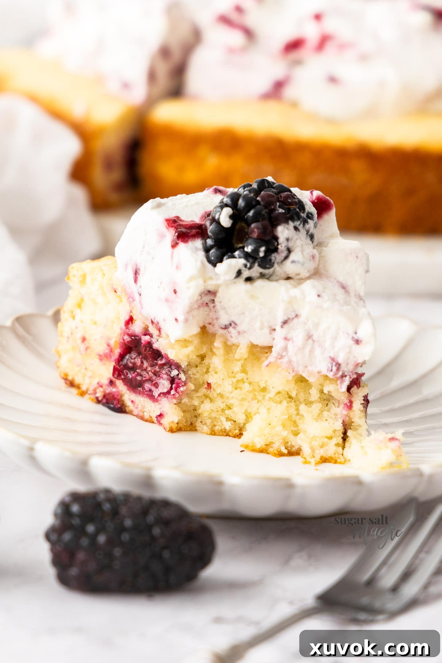 A slice of moist lemon blackberry cake on a plate with a fork, showing the tender crumb and fruit.