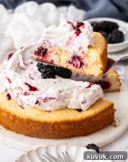 A slice of lemon blackberry cake being lifted from the whole cake with a server.