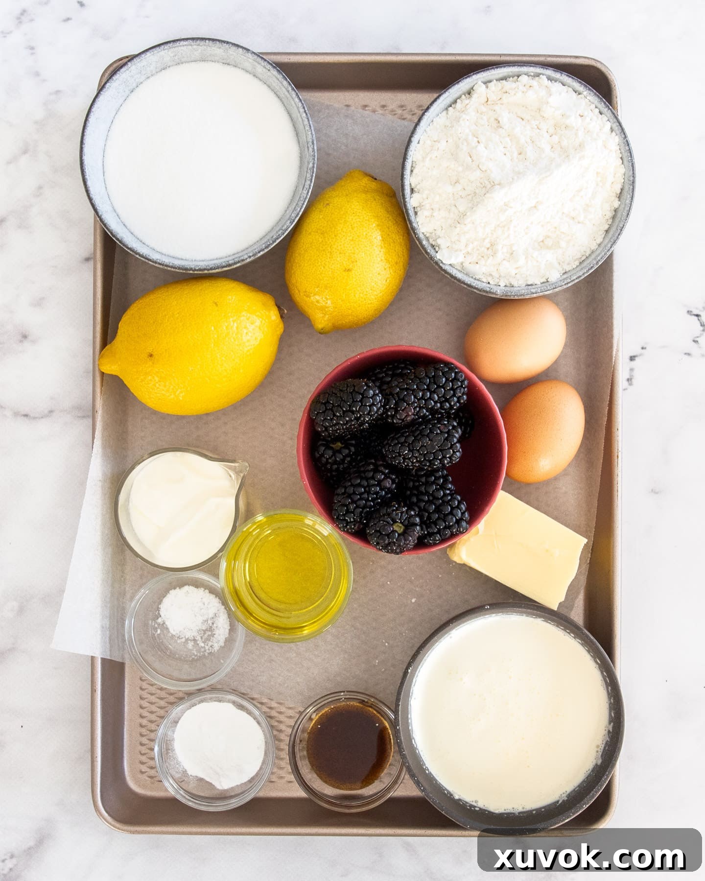 A collection of fresh ingredients for lemon blackberry cake, including lemons, blackberries, and baking essentials, arranged on a baking tray.