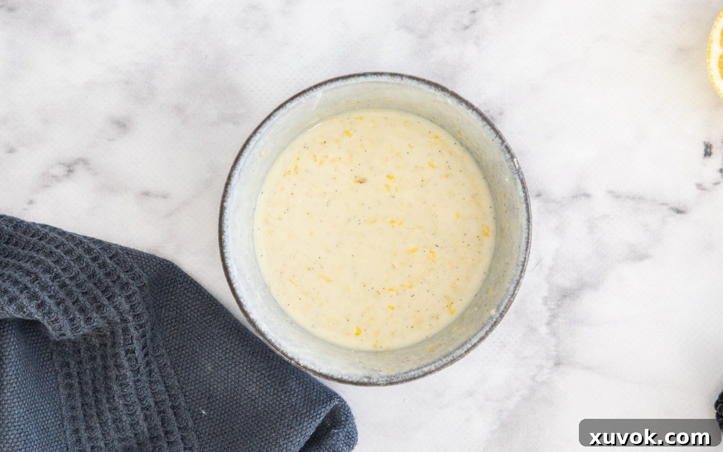 A bowl containing the mixed wet ingredients: yogurt, lemon juice, lemon zest, and vanilla, for the lemon blackberry cake.