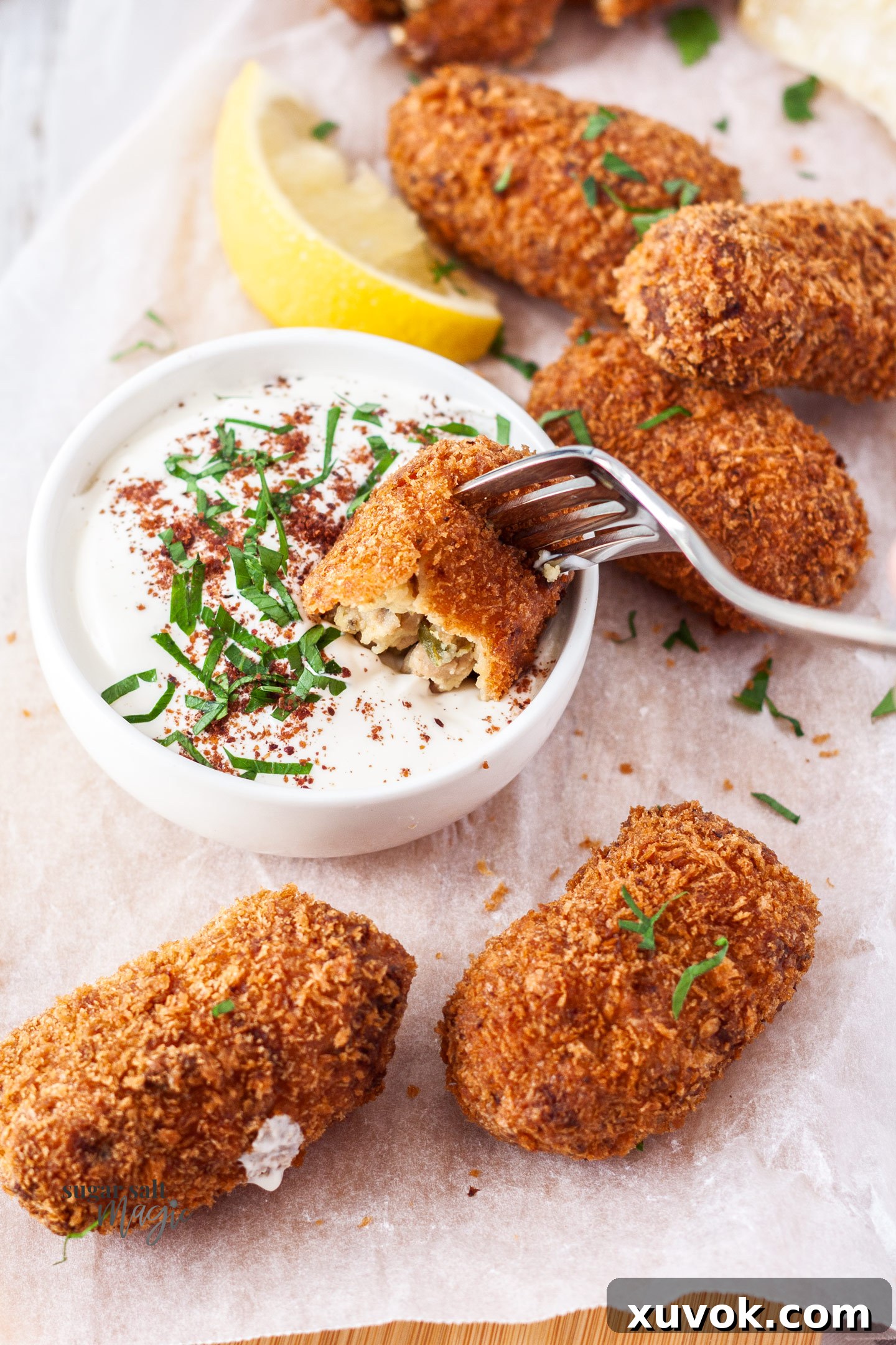 A golden-brown pork croquette being dipped into a creamy white sauce.