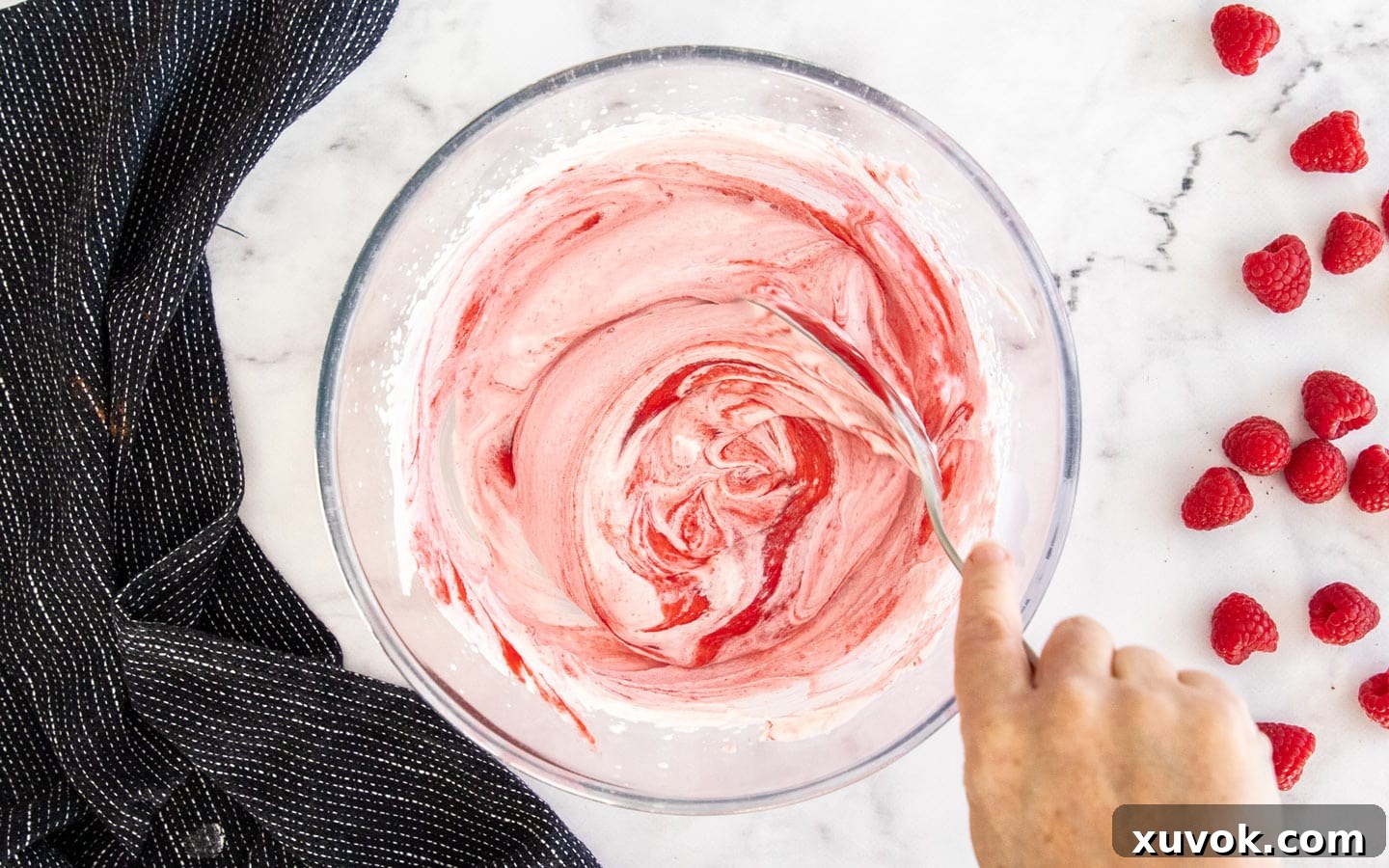 Folding raspberry puree into whipped cream with a spatula.