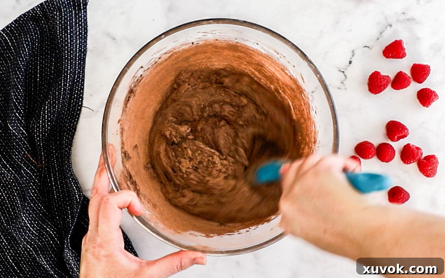 Cocoa powder and flour being mixed into the brownie batter with a spatula.