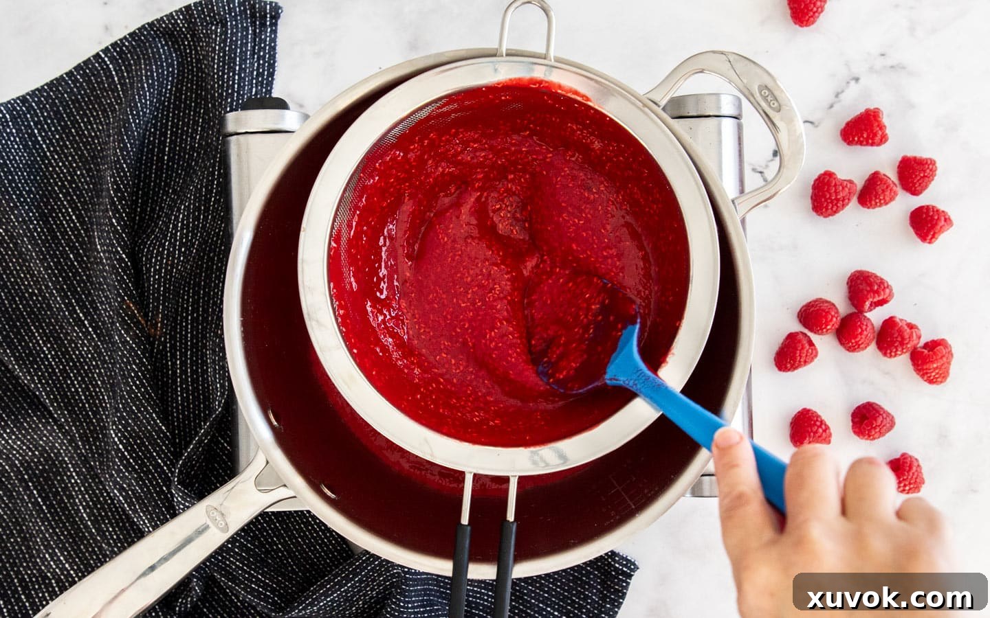 Raspberry puree being strained through a fine-mesh sieve to remove seeds.