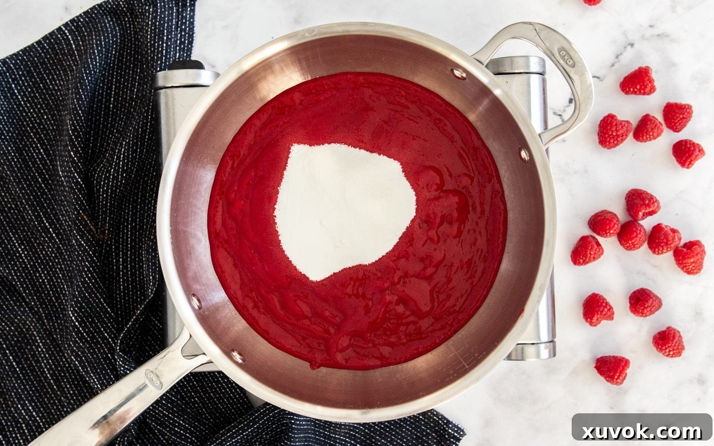 Raspberry puree with granulated sugar stirred in, in a saucepan.