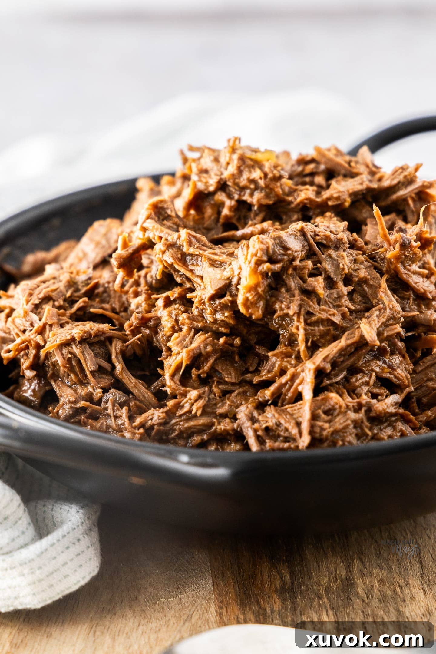 Pulled beef piled high in a black bowl, garnished with fresh herbs.