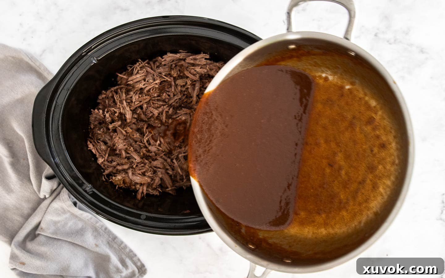 Pouring the rich, thick gravy over the shredded beef in the slow cooker.