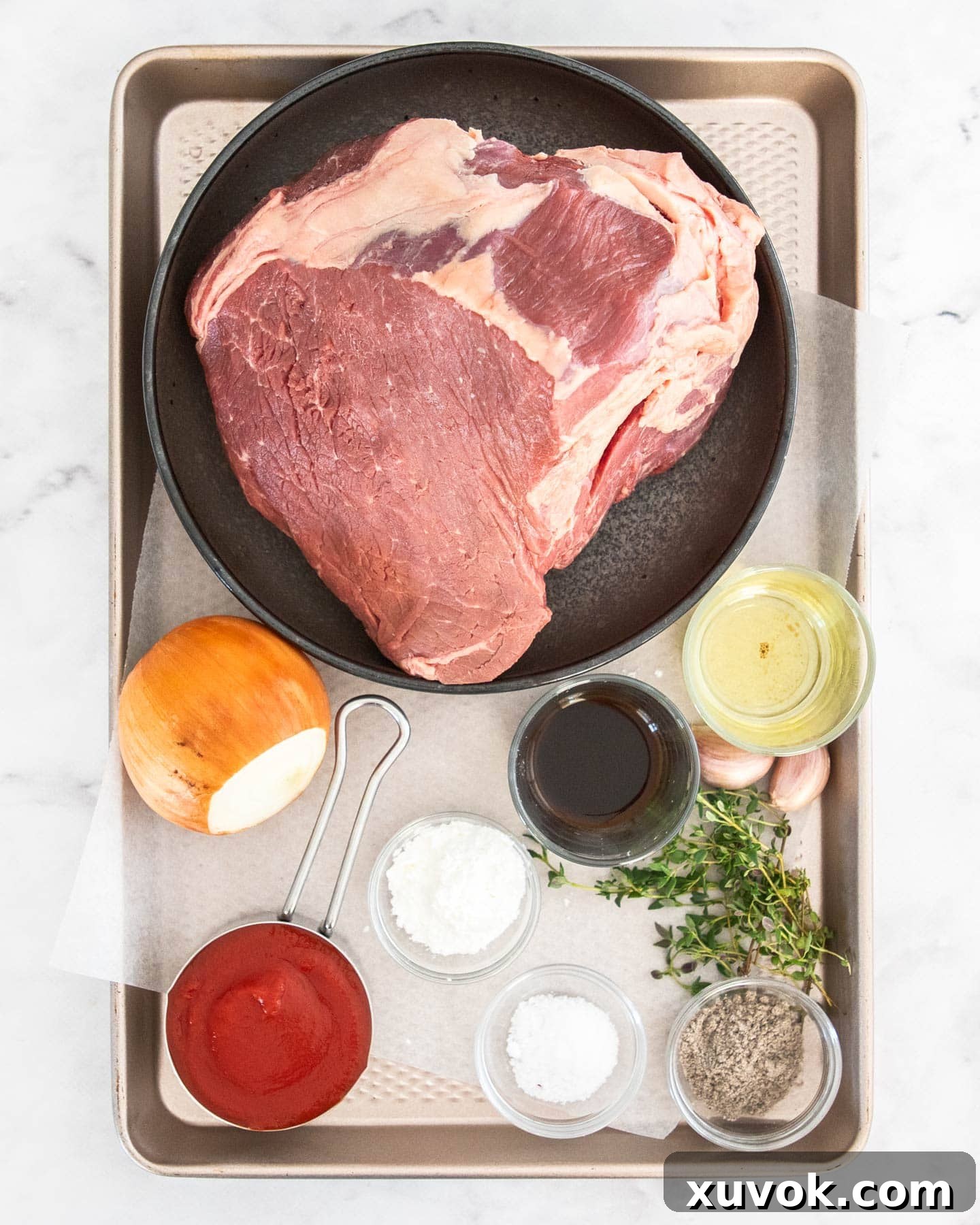 Ingredients for pulled beef on a baking tray, including a beef roast, onions, and herbs.