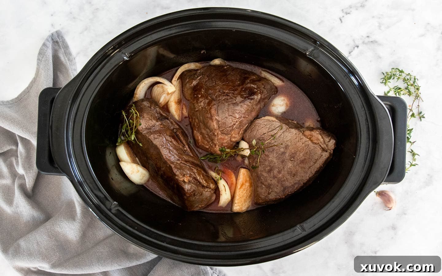 Chunks of beef and sliced onion submerged in sauce in a slow cooker before cooking.