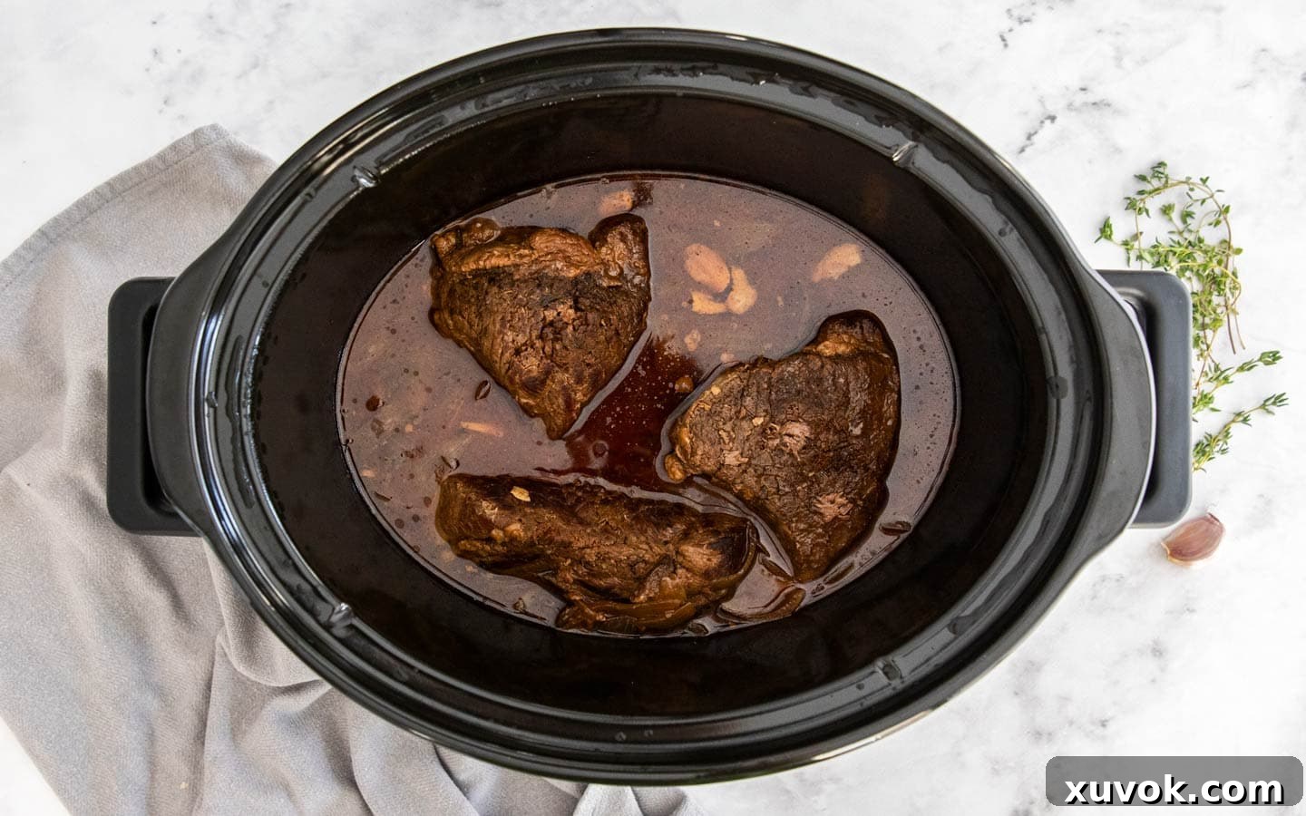 Cooked beef still in its rich sauce within the slow cooker, after hours of slow cooking.