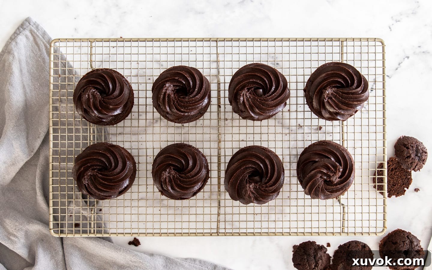 Beautifully frosted mini chocolate cakes, each topped with a delicate swirl of chocolate fudge frosting, ready for decoration.