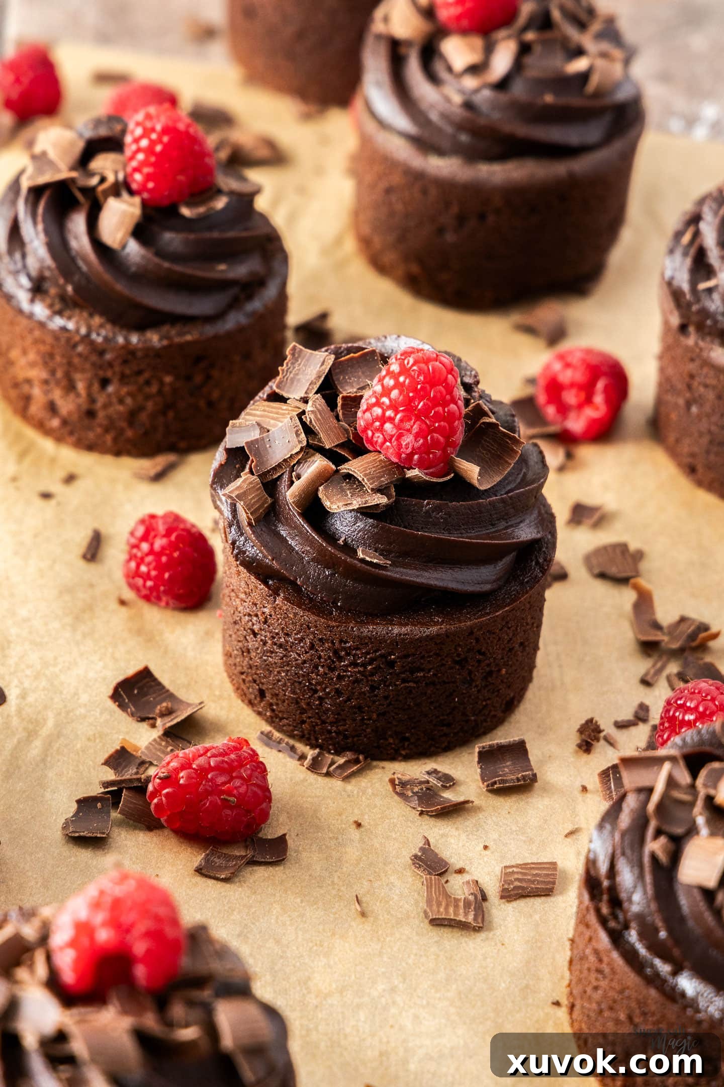 A batch of exquisitely decorated mini chocolate cakes arranged neatly on a sheet of parchment paper.