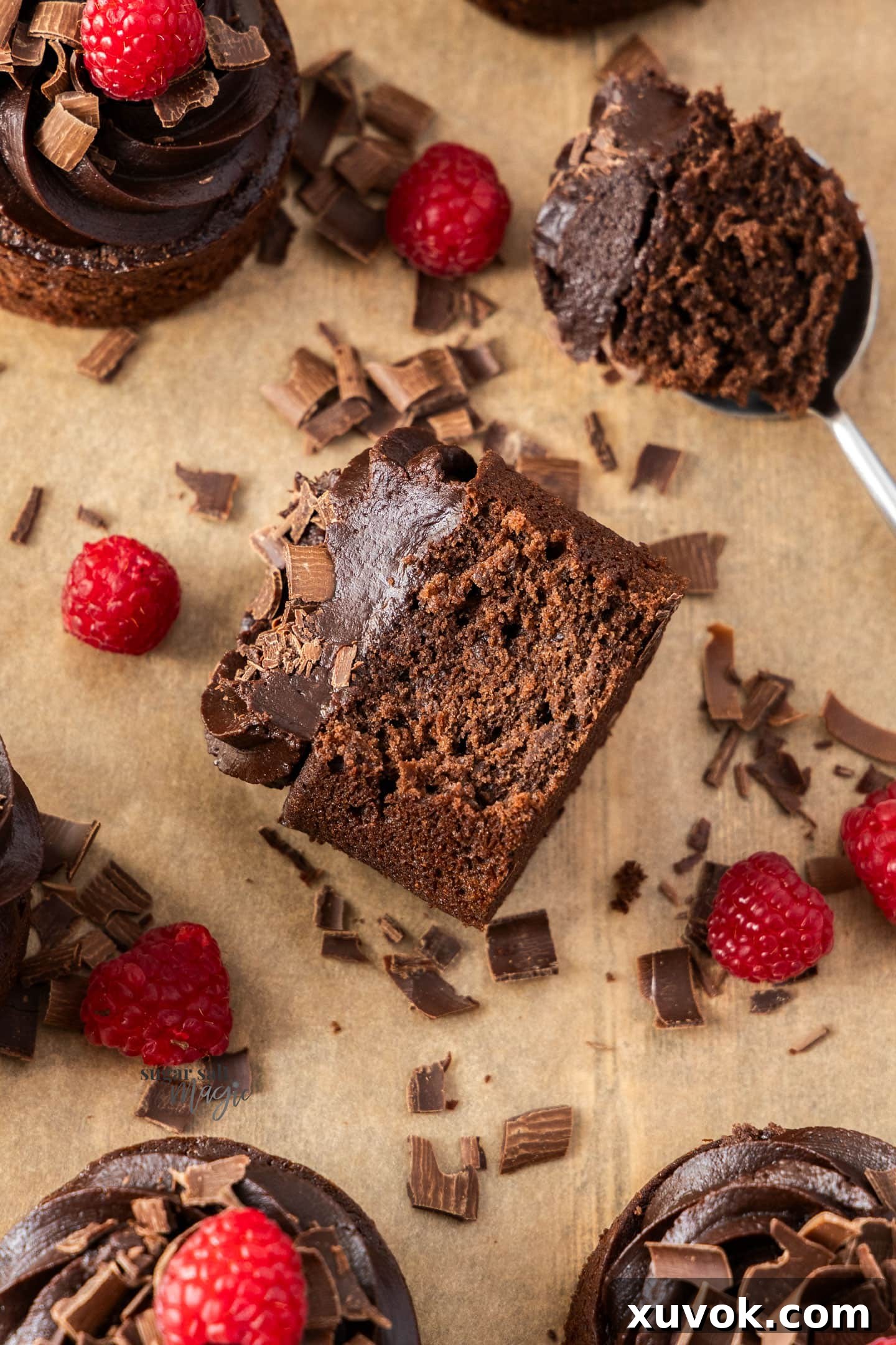 A chocolate mini cake turned on its side, showing a spoonful removed, revealing its moist interior and generous frosting.