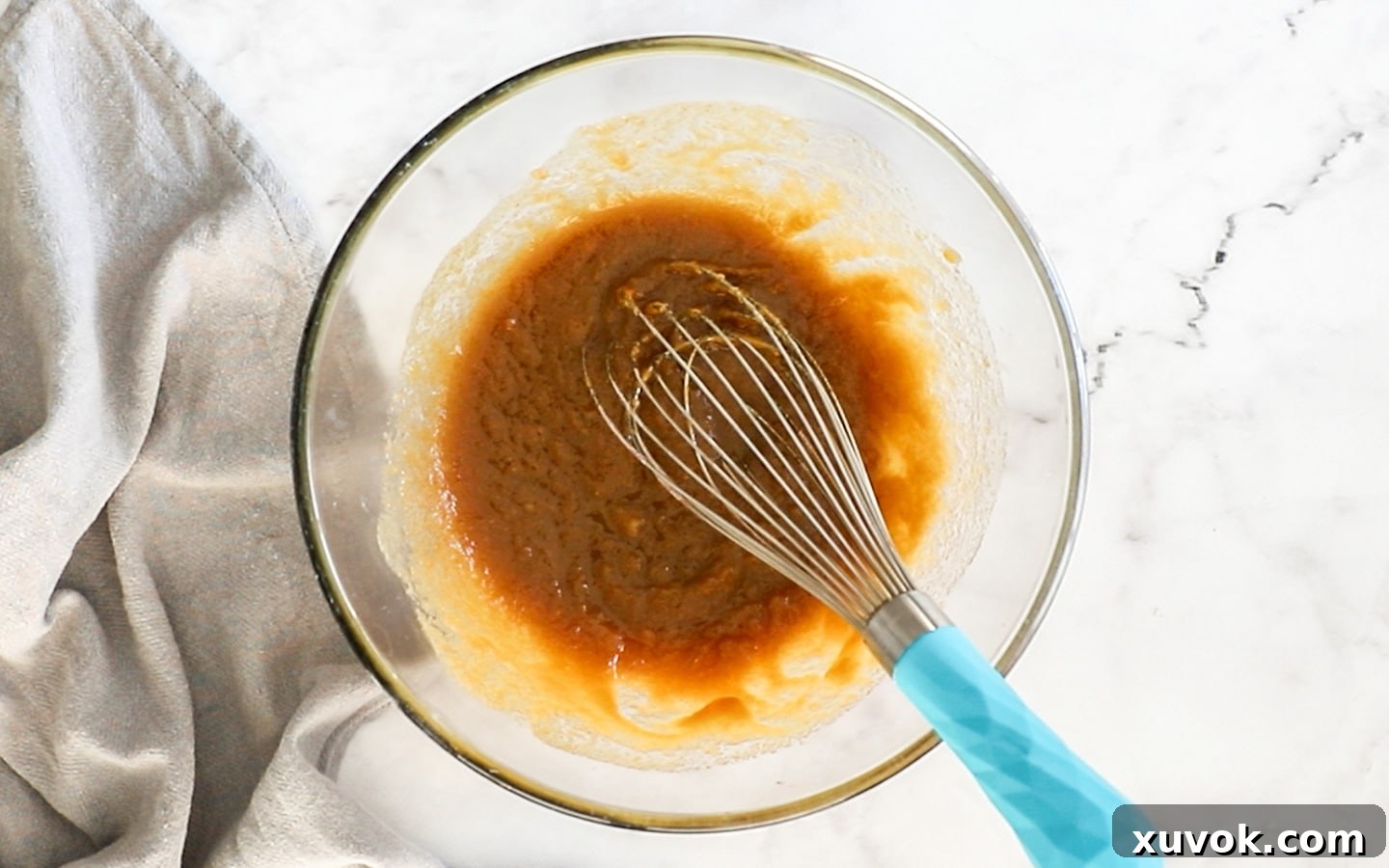 Melted butter and sugars being whisked together in a bowl, creating a light, creamy mixture.