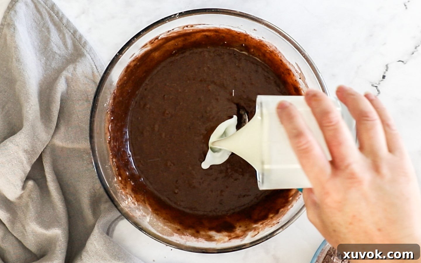 Buttermilk being gently added to the chocolate cake batter, illustrating the alternating wet and dry ingredient method.