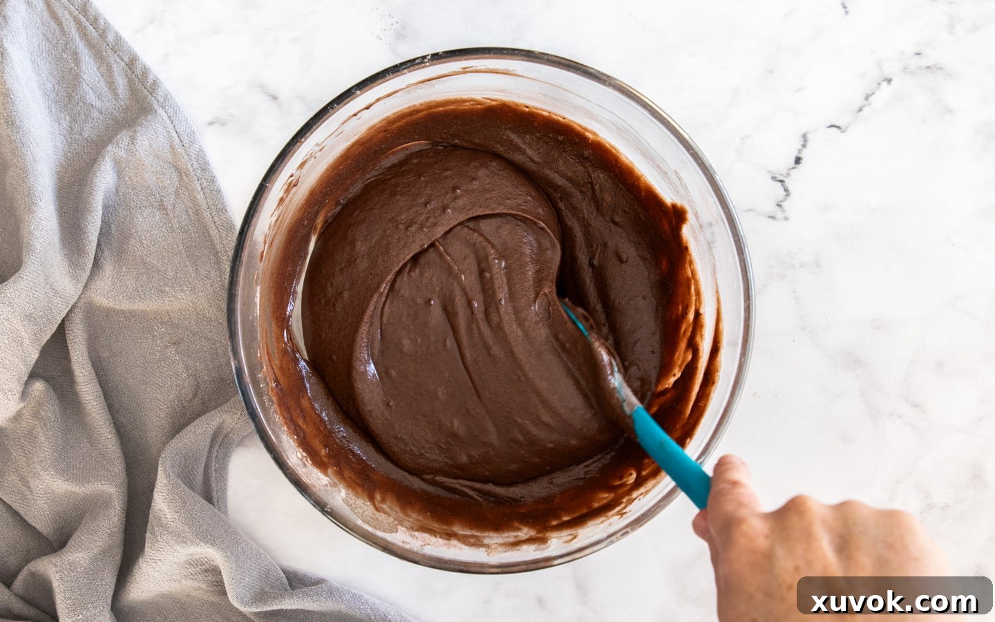 A spatula gently mixing the chocolate cake batter in a bowl, showing the combined wet and dry ingredients.
