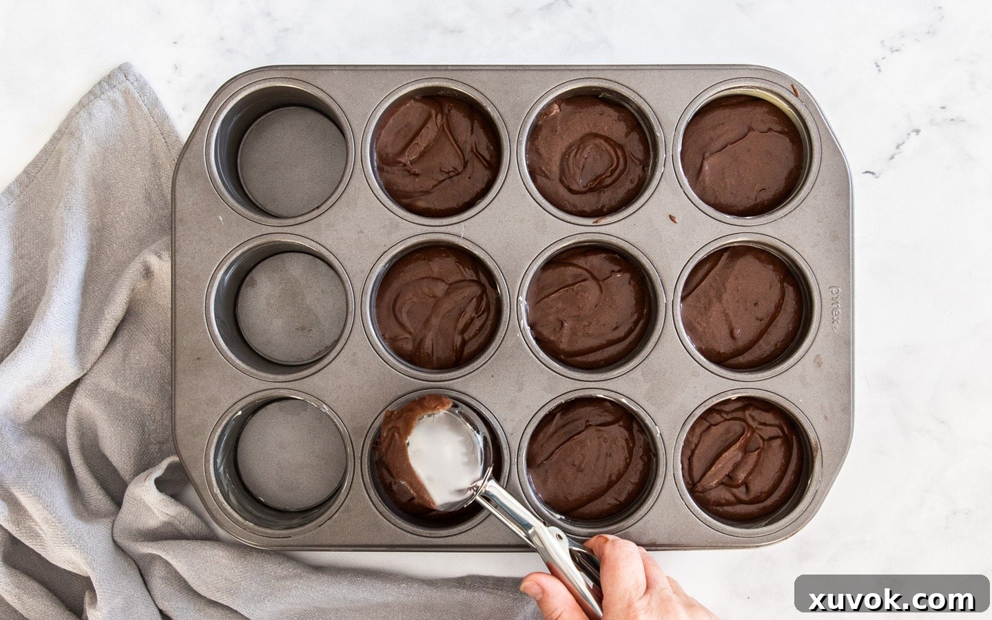Chocolate cake batter being spooned into a mini cheesecake pan, ready for baking.