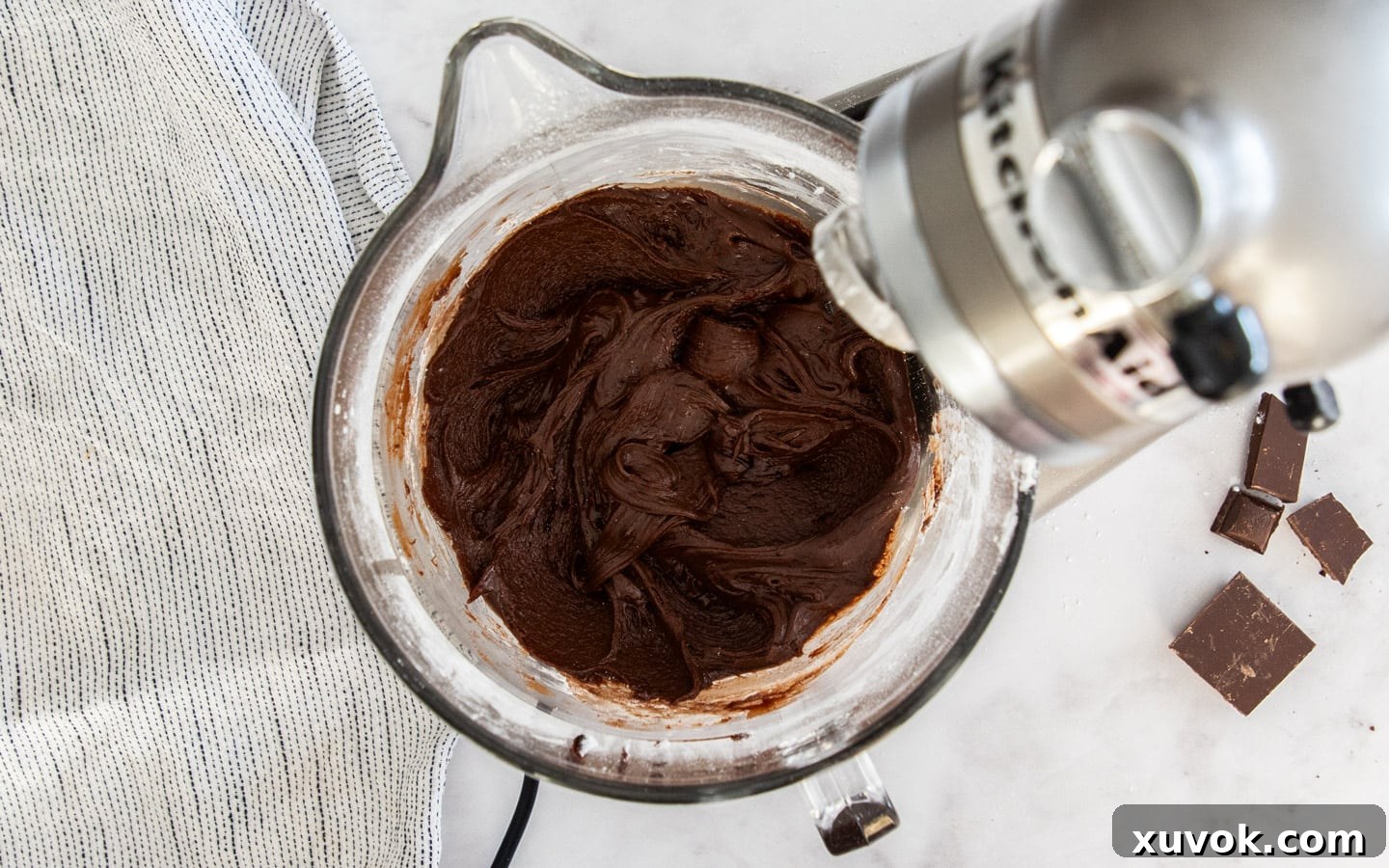Rich chocolate fudge frosting in a stand mixer bowl, showing its smooth, creamy texture.