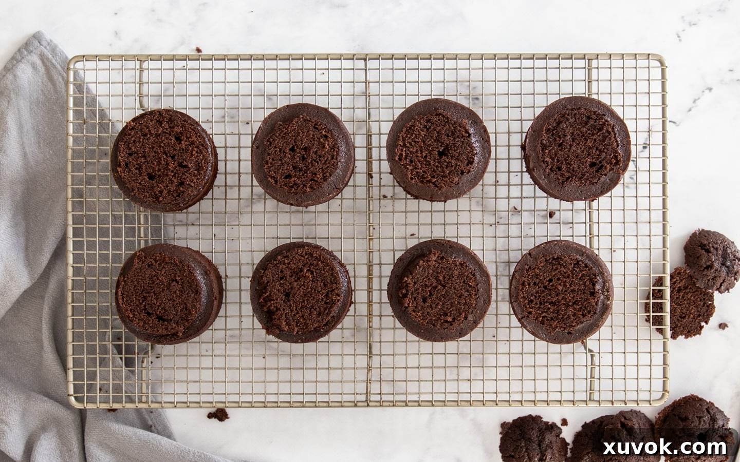 Mini chocolate cakes with their domed tops carefully sliced off, creating a flat surface for frosting.