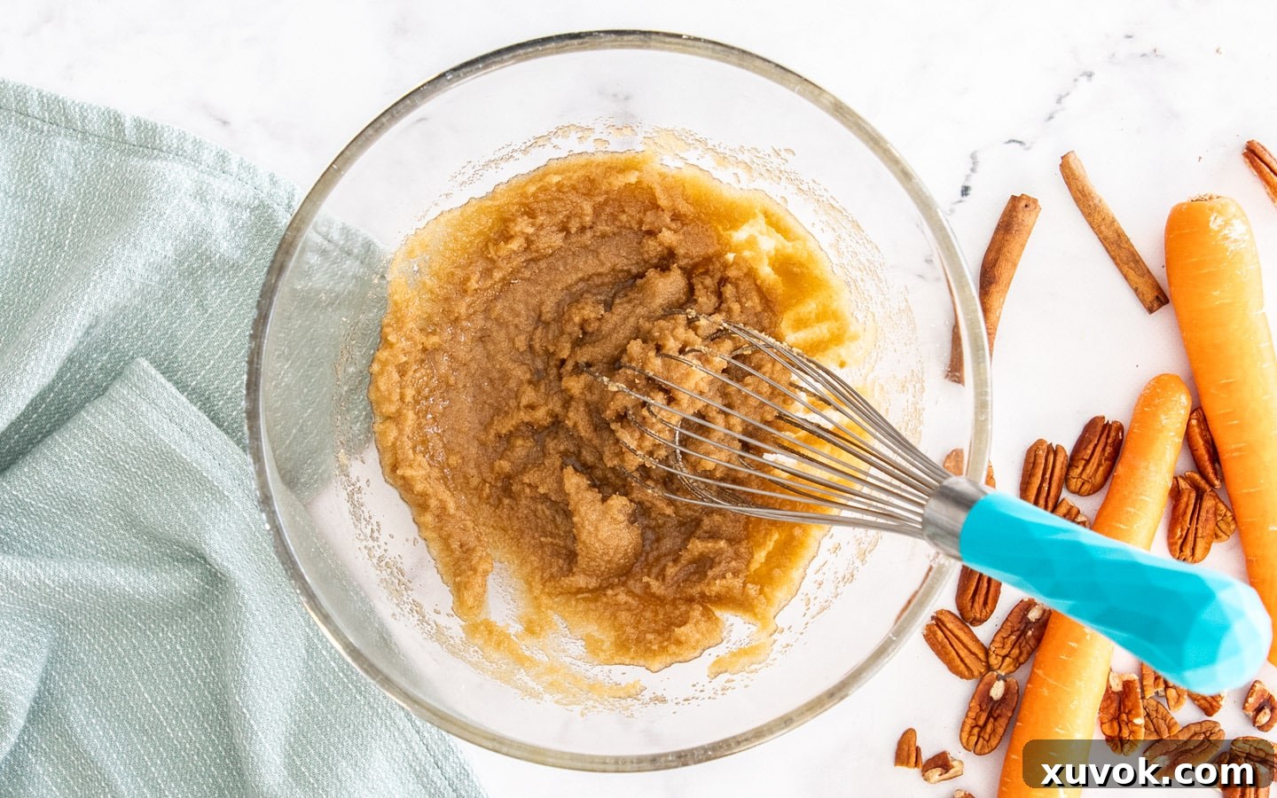 A large mixing bowl with sugar, oil, and melted butter perfectly combined, with a whisk resting in the mixture.