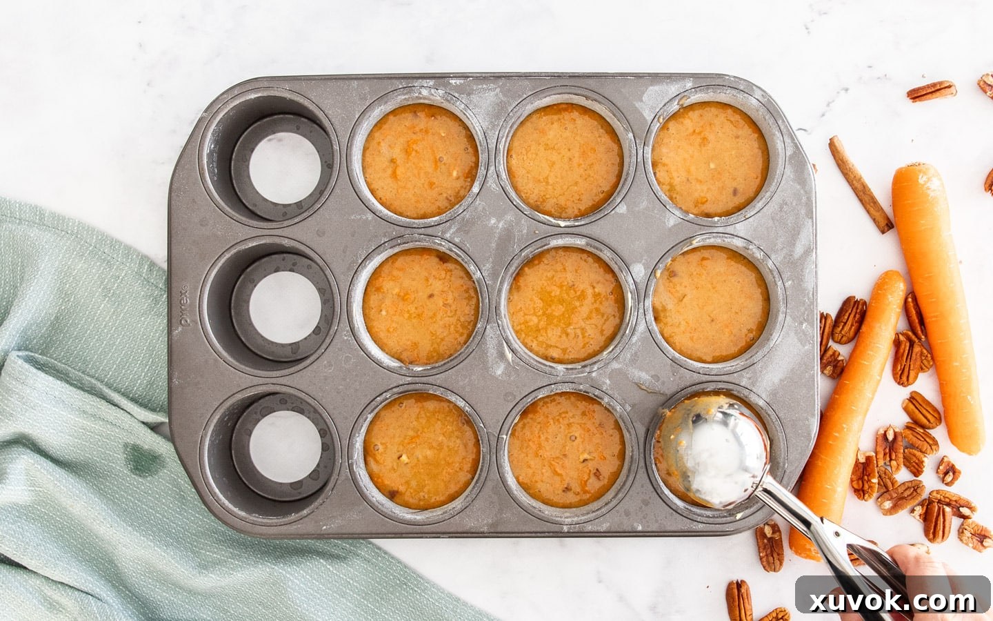 An ice cream scoop adding carrot cake batter into the molds of a mini cheesecake pan, ready for baking.