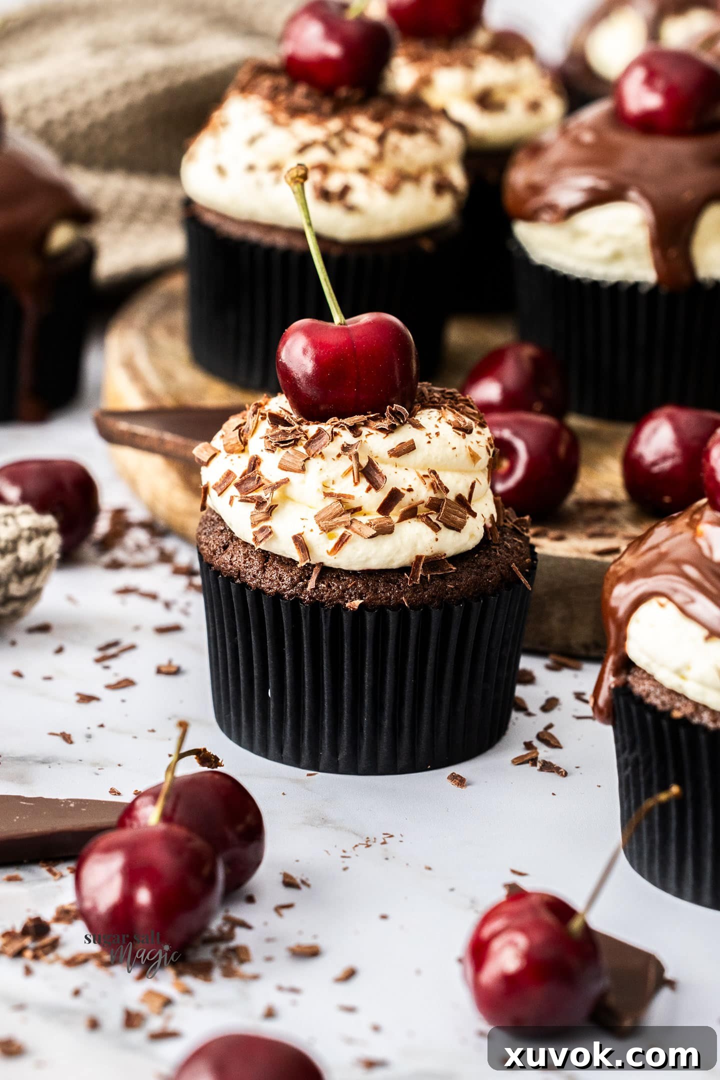 A single black forest cupcake, artfully garnished with chocolate shavings and a fresh cherry.