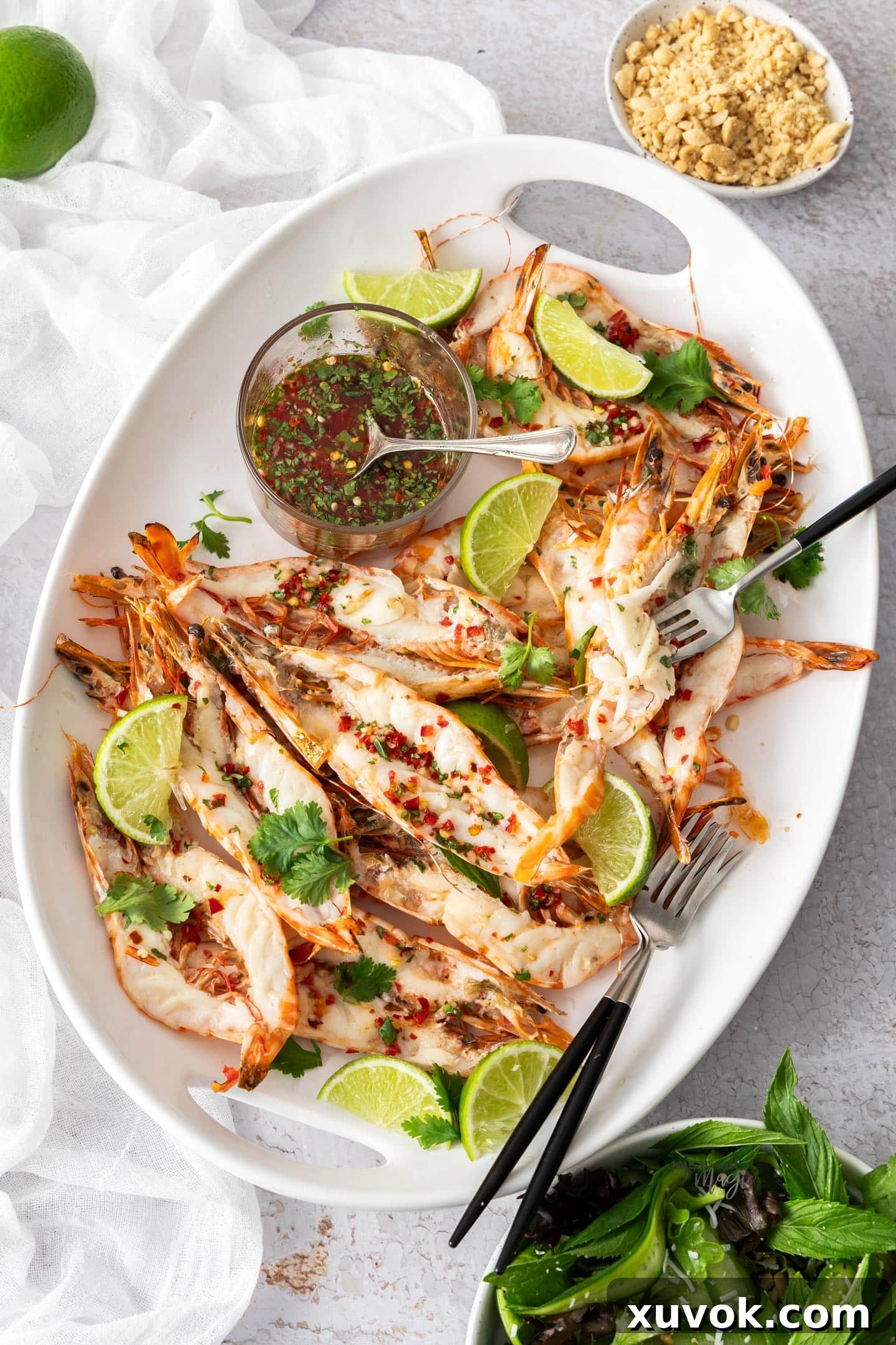 Top down view of butterflied prawns on a large platter with a bowl of Nam Jim dressing.
