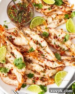 A batch of butterflied prawns on a platter with a small bowl of dressing.