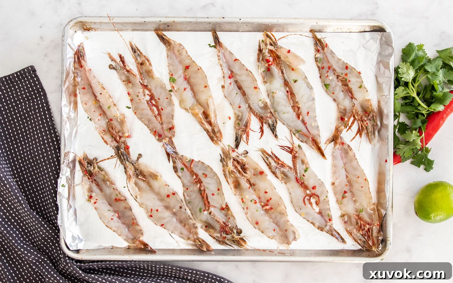 12 butterflied prawns laid out on a baking sheet, ready for grilling.