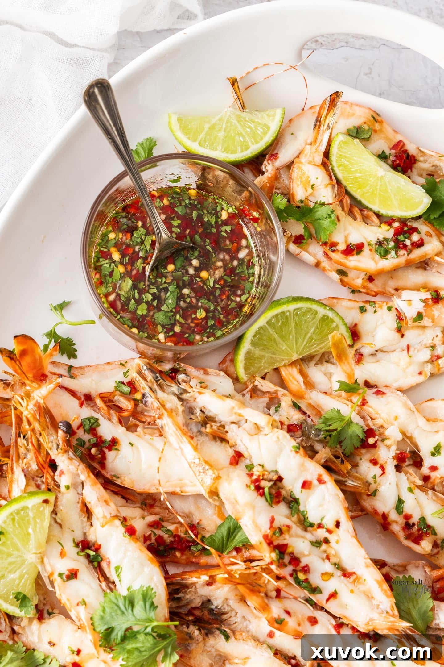 A glass bowl of nam jim sauce surrounded by prawns.