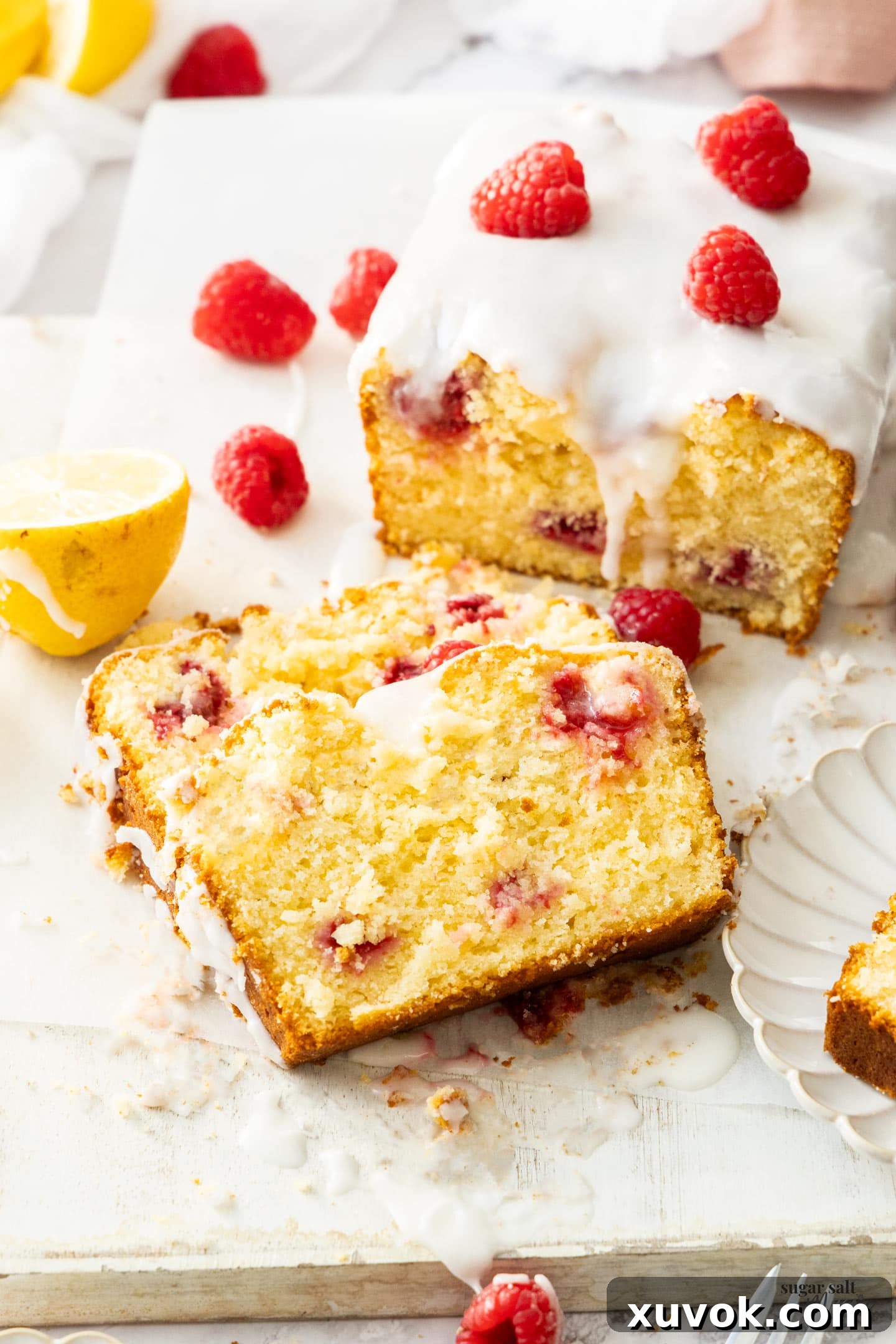 Two slices of vibrant raspberry lemon loaf cake, layered with fresh raspberries and drizzled with a tangy lemon glaze, stacked elegantly on a rustic wooden board.