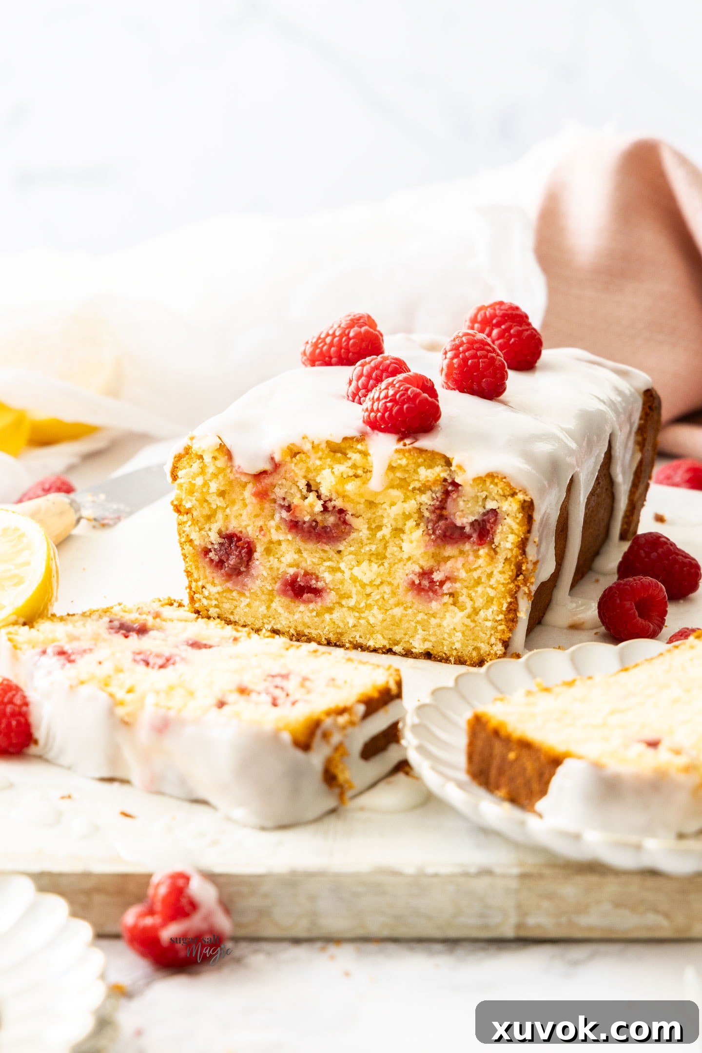 A perfectly baked, golden-brown raspberry lemon loaf cake, studded with bright red raspberries, with one slice elegantly cut away to reveal its moist, tender interior.